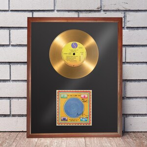 May include: A framed gold record display featuring a metallic gold vinyl disc with a yellow center label positioned above a square album cover art print titled Speaking in Tongues by Talking Heads, which includes several black ink signatures.