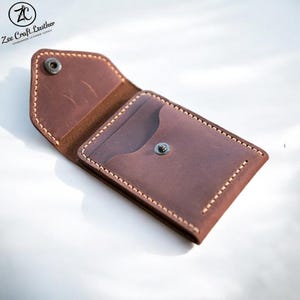 May include: Open brown leather card holder with a snap closure. The wallet has a pocket and is stitched with light-colored thread. The brand name "Zee Craft Leather" is visible in the upper left corner.