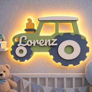 Può includere: Una lampada da parete a forma di trattore verde con ruote blu scuro e tetto bianco. Il nome Lorenz è scritto in corsivo bianco al centro della carrozzeria del trattore. L'oggetto emette una luce calda dai bordi posteriori.