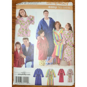 May include: A Simplicity sewing pattern envelope labeled 3575 featuring illustrations of hooded robes in various colors and patterns. The front displays a blue robe, a pink robe with green frog prints, a solid red robe, and a rainbow striped robe.