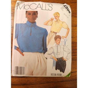 May include: A McCall's 2208 sewing pattern envelope for sizes 14-16-18. The front features illustrations of three blouse variations: a blue high-neck blouse with buttons, a yellow short-sleeve blouse, and a white long-sleeve blouse with a neck tie.