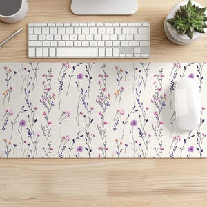 May include: A rectangular mouse mat with a floral design. The pattern shows purple, pink, and orange flowers with green stems on a cream backdrop. A white computer mouse is positioned on the right side of the mat.