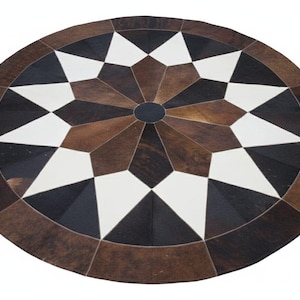 Pode incluir: Tapete redondo de pele de vaca com um padrão geométrico de estrela. O tapete apresenta um círculo preto central, rodeado por formas geométricas brancas, pretas e castanhas, e uma borda castanha escura. Diâmetro: aprox. 150 cm.