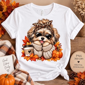 Peut inclure: Un t-shirt blanc avec une illustration d'un chien poilu portant des lunettes de soleil à motif léopard et un bandeau assorti, vêtu d'un pull beige. Le chien tient un gobelet à café avec un cœur, entouré de feuilles d'automne et d'une citrouille.