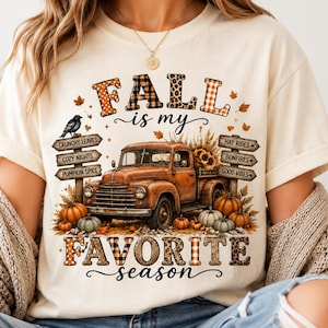 Peut inclure: Un t-shirt crème avec un motif de camion vintage orange entouré de citrouilles, de tournesols et de feuilles d'automne. Le texte indique "FALL is my FAVORITE season" avec des panneaux listant "CRUNCHY LEAVES," "COZY NIGHTS," "PUMPKIN SPICE," "HAY RIDES," "BONFIRES," et "GOOD VIBES."