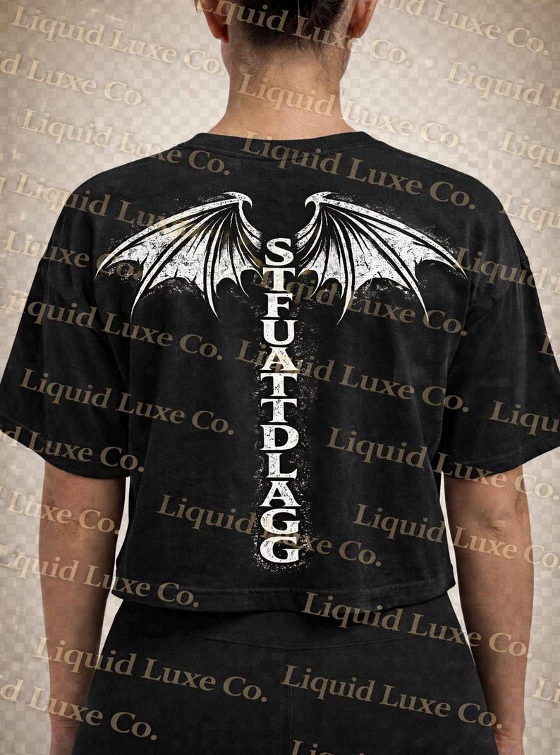 May include: Black crop top with a white graphic of stylized wings and the text "STFUATTDLAGG" in a vertical column. The shirt is made of a soft material and has short sleeves. The overall theme is edgy and alternative.