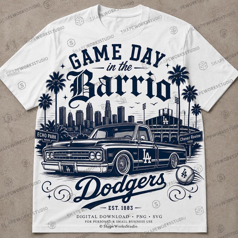 May include: White t-shirt featuring a navy blue graphic design. The design includes the text "Game Day in the Barrio" above a vintage truck, the word "Dodgers", and a baseball. The shirt also has the text "Est. 1883".