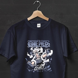 May include: A dark navy blue short-sleeved t-shirt featuring a graphic print of the character Monkey D. Luffy in Gear 5 form. The design includes the text ONE PIECE, GEAR 5, and MONKEY D. LUFFY, surrounded by stylised white clouds and smoke elements.
