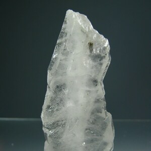 Puede incluir: Un cristal de cuarzo transparente con una punta puntiaguda y una base plana. El cristal es translúcido y tiene una ligera apariencia lechosa. Mide aproximadamente 12,5 cm de alto.