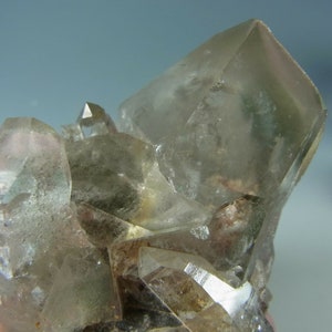 Puede incluir: Un grupo de cristales de cuarzo transparentes con un tono gris ahumado. Los cristales son afilados y bien formados, con una variedad de tamaños y formas.