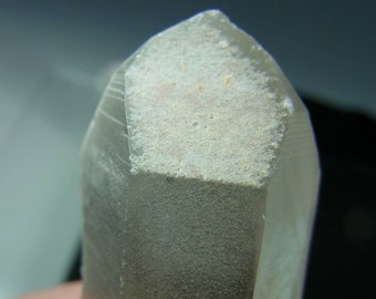 Puede incluir: Un cristal de cuarzo transparente con una parte superior helada y nublada. El cristal es puntiagudo en la parte superior y tiene una forma hexagonal.
