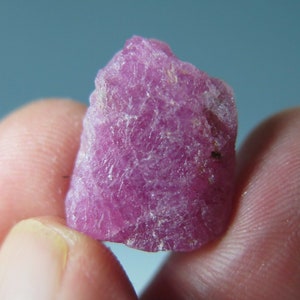 May include: A rough, pink ruby crystal with a pointed top and a textured surface.