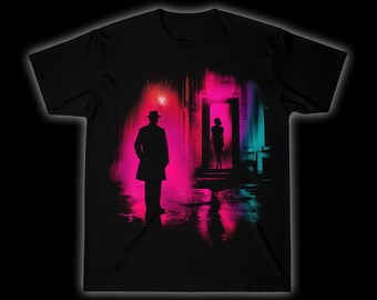 Op de afbeelding: Zwart T-shirt met een neon straatbeeld. Een man met hoed en jas staat op de voorgrond, met een vrouw in een deuropening op de achtergrond. De scène is weergegeven in roze, blauw en zwart.