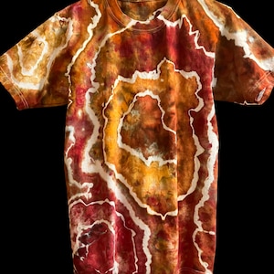 Pode incluir: Uma t-shirt de manga curta com um padrão tie-dye em espiral em tons de vermelho, laranja e amarelo, com detalhes em branco. A t-shirt tem gola redonda e um corte padrão. O design tie-dye cria um visual artístico único.