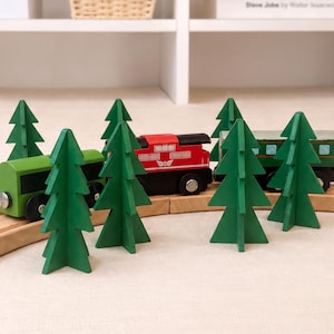 May include: A wooden toy train set featuring a red locomotive and green passenger cars on a curved wooden track. Several green, flat, stylised wooden pine trees are arranged around the train. The train has black wheels and silver connectors.