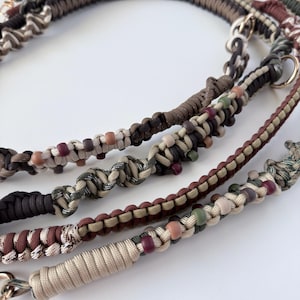 May include: Close-up of several dog leashes in various shades of brown, beige, and green. The leashes are made of braided cord and feature decorative beads. Each leash has a metal clasp.