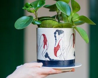 Hand-painted ceramic planter with sequential illustrations of a forward roll with a drainage hole and saucer