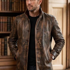 May include: A brown distressed leather jacket with a high collar, long sleeves, and a button-front closure. The jacket features a weathered texture with darker brown patches and two side pockets. It is worn over a plain black shirt and dark jeans.