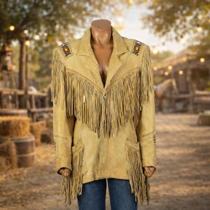 Peut inclure: Veste en daim beige avec de longues franges sur le devant, le dos et les manches. La veste présente des perles décoratives sur les épaules et les poches. La veste est présentée sur un mannequin, avec un arrière-plan extérieur flou.