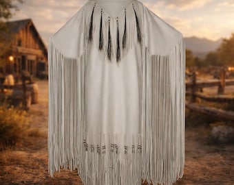 May include: A cream-coloured, fringed dress with long sleeves and a V-neckline. The dress has black fringe accents at the neckline and hem, and long fringe along the sleeves. The dress is displayed on a mannequin.