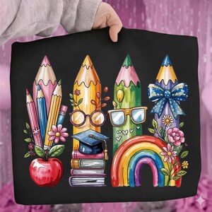 Puede incluir: Bolso tote negro con una colorida ilustraci&oacute;n de l&aacute;pices, una manzana, libros, un gorro de graduaci&oacute;n y un arco&iacute;ris. Los l&aacute;pices son de varios colores y est&aacute;n decorados con flores y gafas. Un dise&ntilde;o divertido para profesores o estudiantes.