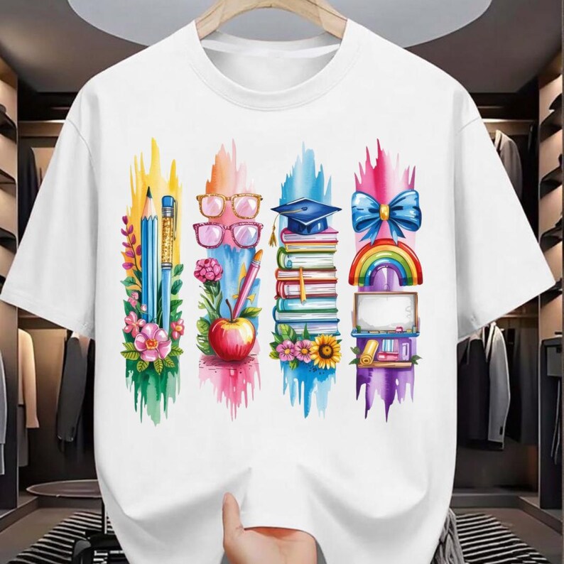 Puede incluir: Camiseta blanca con un dise&ntilde;o gr&aacute;fico colorido. El dise&ntilde;o incluye un l&aacute;piz, gafas, un birrete, un lazo, un arco&iacute;ris, libros, flores y una manzana. El gr&aacute;fico est&aacute; sobre pinceladas verticales en varios colores.