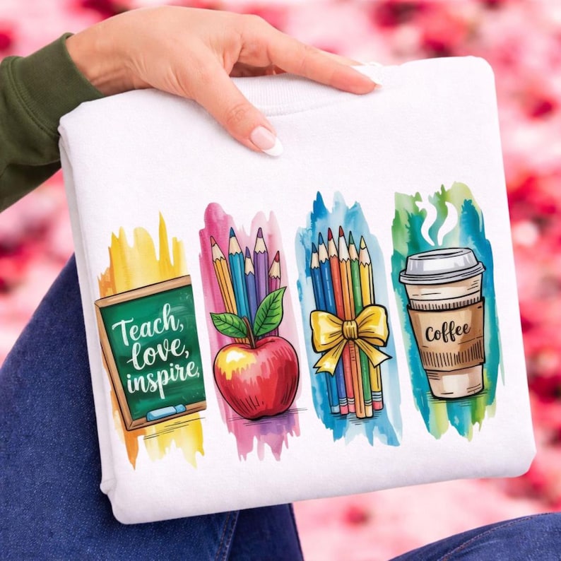 Puede incluir: Sudadera blanca con ilustraciones coloridas relacionadas con la escuela. El dise&ntilde;o incluye una pizarra con las palabras "Teach, love, inspire", una manzana roja, l&aacute;pices y una taza de caf&eacute;. La obra de arte est&aacute; sobre fondos de estilo acuarela.
