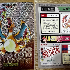 Può includere: Carta collezionabile Pokémon olografica con Charizard, creatura arancione e blu simile a un drago, con fiamme. Testo giapponese visibile, insieme alle parole "POCKET MONSTER".