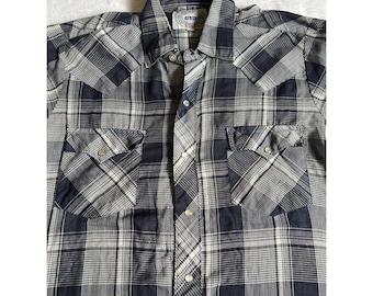 May include: A button-down plaid shirt in shades of navy blue, white, and gray. The shirt features two chest pockets with button closures and a classic collar. The fabric has a woven texture.