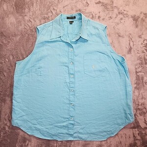 May include: A sleeveless, light blue button-down shirt. The shirt has a collar, a single chest pocket with a small logo, and a button-up front. The fabric appears to be linen or a similar lightweight material.