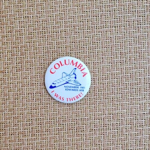 May include: A white button with the word "COLUMBIA" in red, and a blue and white illustration of a space shuttle. The text "NOVEMBER 1981 EDWARDS AFB" and "I WAS THERE!" are also present.