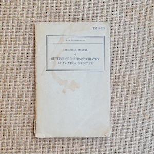 May include: A vintage technical manual titled "Outline of Neuropsychiatry in Aviation Medicine" from the War Department. The cover is off-white with black text and a rectangular border. The manual shows signs of age with some staining.