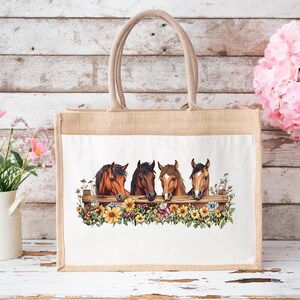 May include: A beige tote bag with a white panel featuring a watercolor illustration of four horse heads peering over a wooden fence adorned with colorful flowers. The bag has a sturdy, woven handle.