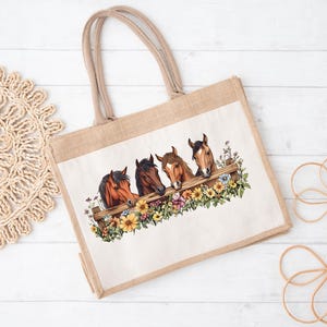 May include: A beige tote bag with a rectangular image of four horse heads peeking over a wooden fence. The fence is surrounded by colorful flowers. The bag has two beige handles and is made of a natural-looking material.