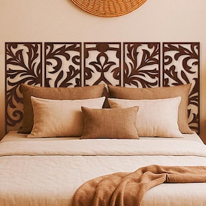 May include: A bedroom scene featuring a wooden bed frame with a beige comforter and pillows. A decorative headboard with a floral design is above the bed. A woven wall hanging and two wooden nightstands with lamps complete the warm, inviting space.