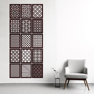 Può includere: Un set di dodici pannelli decorativi marrone scuro con vari motivi geometrici. I pannelli sono montati su una parete bianca, mostrando una gamma di design tra cui cerchi, linee e motivi floreali. Una moderna sedia grigia e un arredamento minimalista sono sullo sfondo.
