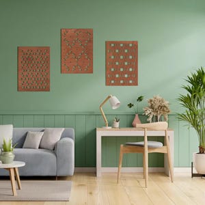 Può includere: Tre pannelli di arte murale in legno con intricati disegni ritagliati. I pannelli sono di varie forme e dimensioni, con una finitura marrone caldo. L'arte è esposta su una parete verde, creando un'estetica moderna e naturale. La stanza comprende anche una scrivania, una sedia e un divano.