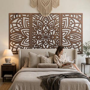 May include: A three-panel dark brown wooden wall art piece featuring an intricate laser-cut mandala pattern. The rectangular panels are mounted horizontally above a bed, displaying symmetrical geometric shapes and floral-inspired cutouts.
