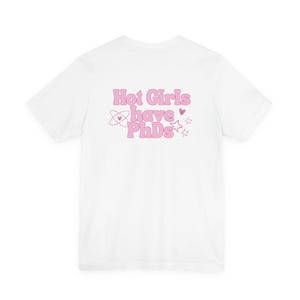 May include: White t-shirt with the phrase "Hot Girls have PhDs" in pink lettering. The design includes an atom symbol, a heart, and stars. The shirt is a casual wear item.