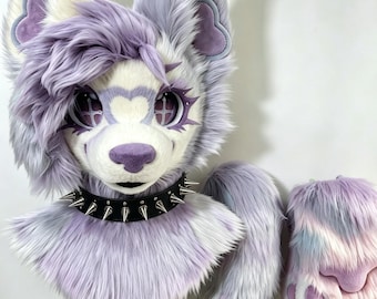 Könnte beinhalten: Eine Tierkopfmaske aus Kunstfell mit langem, lavendelfarbenem, weißem und grauem Synthetikfell, großen spitzen Ohren mit violetten Akzenten und einem schwarzen Stachelhalsband. Die Maske hat große Augen mit kreuzförmigen Pupillen.