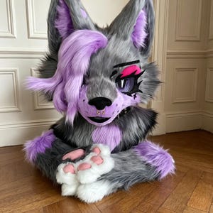 May include: A grey and purple faux fur animal head mask with large pointed ears, a side-swept purple fringe, and long eyelashes. The mask features a black nose, a septum piercing, and white paw-like hands resting in front of the chest area.