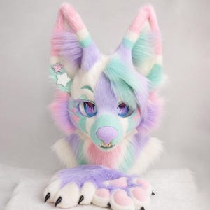 May include: A pastel-colored faux fur animal head mask featuring large pointed ears, purple, pink, and mint green fur, and two star-shaped hair clips. The mask has large expressive eyes, a purple nose, and a matching pair of furry paw gloves.