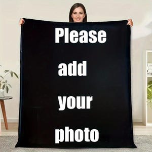 May include: A large black blanket with the words "Please add your photo" in white block letters. A woman is holding the blanket up, smiling at the camera. The blanket is displayed indoors.