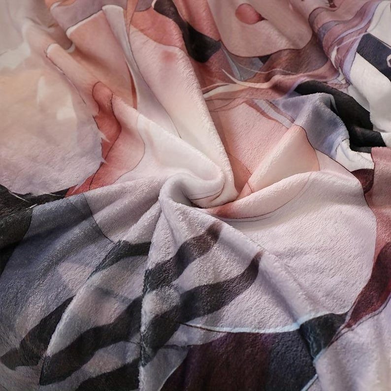 May include: A soft, plush blanket with a detailed, artistic design. The blanket features a blend of colors, including pink, white, gray, and black. The design appears to be an abstract illustration or a stylized portrait, with flowing lines and shapes.