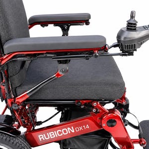 Op de afbeelding: Een Rubicon DX14 elektrische rolstoel met een glanzend rood metalen frame, een zwart gestoffeerde zitting en zwarte armleuningen. De stoel is voorzien van een joystickbedieningsmodule op de rechterarmleuning en een zwarte voetplaat.