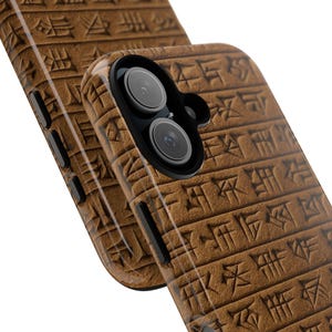 May include: Close-up of two brown phone cases with a textured surface and a pattern of ancient writing. One case has a camera lens. The cases are angled, showing the side buttons and the camera lens.