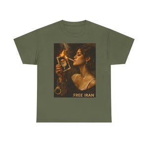 Puede incluir: Camiseta verde oliva con un gráfico de una mujer fumando un cigarrillo mientras sostiene una fotografía en llamas. La imagen incluye el texto "FREE IRAN" en la parte inferior. La mujer lleva un top blanco y esposas.