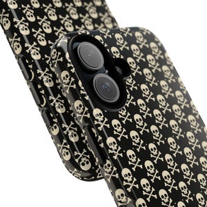 May include: Black phone case with a repeating pattern of off-white skulls and crossbones. The case has a glossy finish and features camera lenses. The design is a classic symbol of rebellion and alternative culture.
