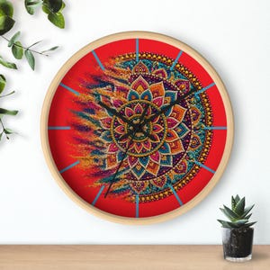 Puede incluir: Un reloj de pared redondo con marco de madera clara, que presenta un fondo rojo vibrante y un diseño de mandala colorido que parece disolverse en partículas en el lado izquierdo. El reloj tiene manecillas negras y marcas azules.