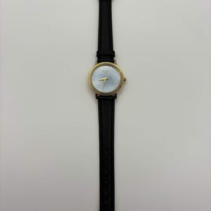 May include: A gold-toned wristwatch with a light blue face and black leather band. The watch has gold hands and a gold bezel. The watch band is thin and has a silver buckle. The watch is centered on a white background.